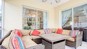 A covered outdoor seating area with wicker furniture, a table, and a view of the interior through glass doors. - Enchanting Dog-friendly Home With Pool, Lanai, Central AC, & Washer/dryer (Kissimmee)