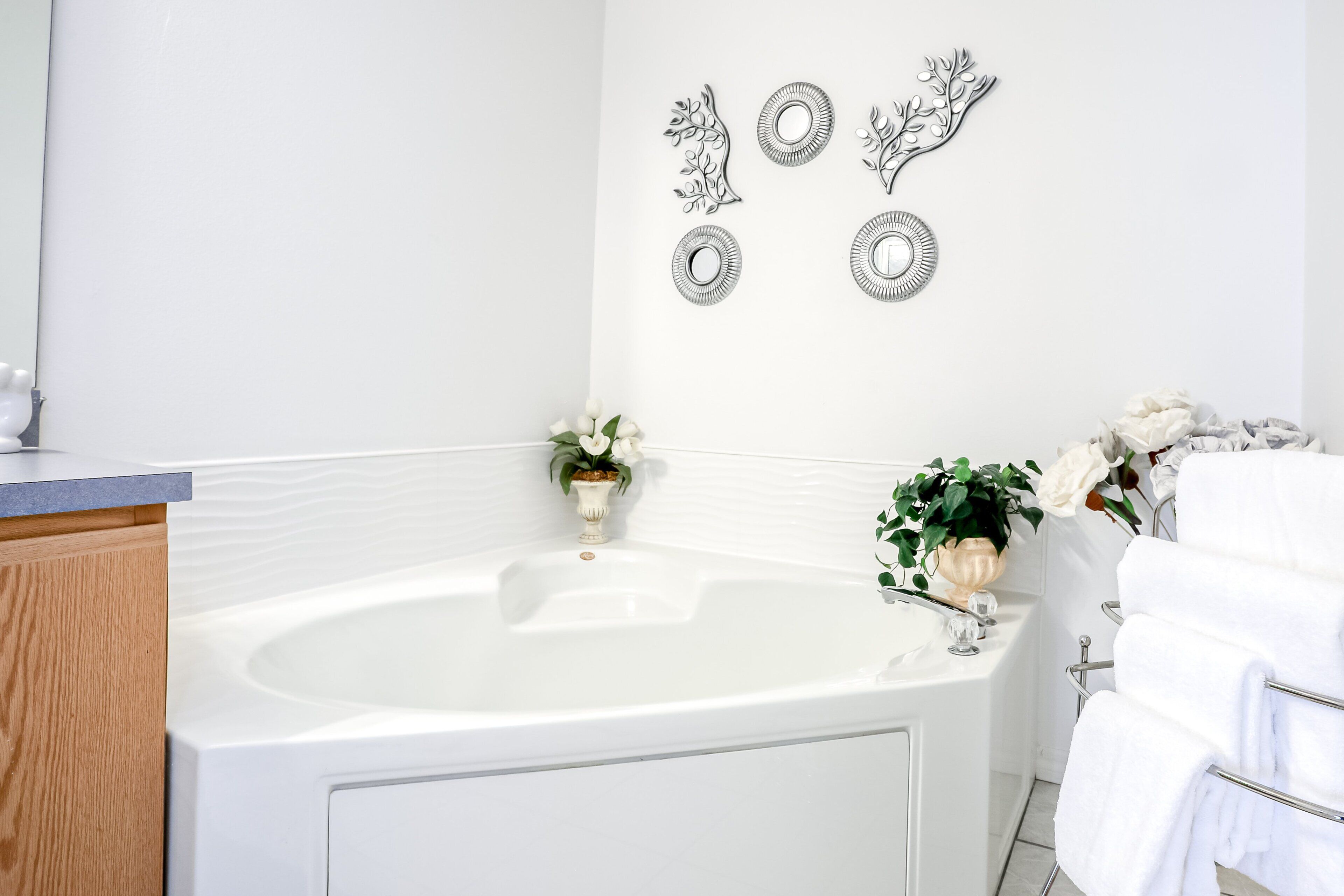 A bathroom with a white bathtub, a wooden vanity, and decorative wall mirrors.