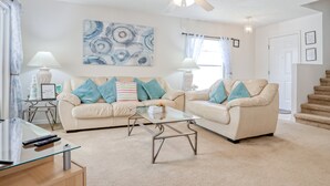 A living room with two sofas, a glass coffee table, and a ceiling fan. - Enchanting Dog-friendly Home With Pool, Lanai, Central AC, & Washer/dryer (Kissimmee)