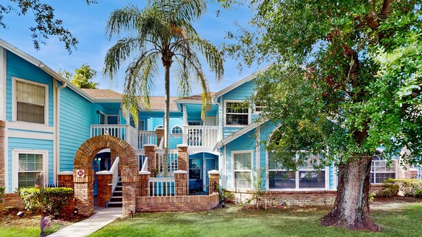 A two-story building with a brick archway entrance, a covered porch, and a large tree in the front yard. - Beautiful Home Boasting Entertainment for Everyone With Wifi (Kissimmee)