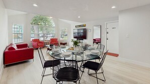 A modern living room with a glass dining table, red and black chairs, a red sofa, and a TV mounted on the wall. - Beautiful Home Boasting Entertainment for Everyone With Wifi (Kissimmee)