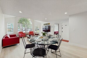 A modern living room with a glass dining table, red and black chairs, a red sofa, and a TV mounted on the wall. - Beautiful Home Boasting Entertainment for Everyone With Wifi (Kissimmee)