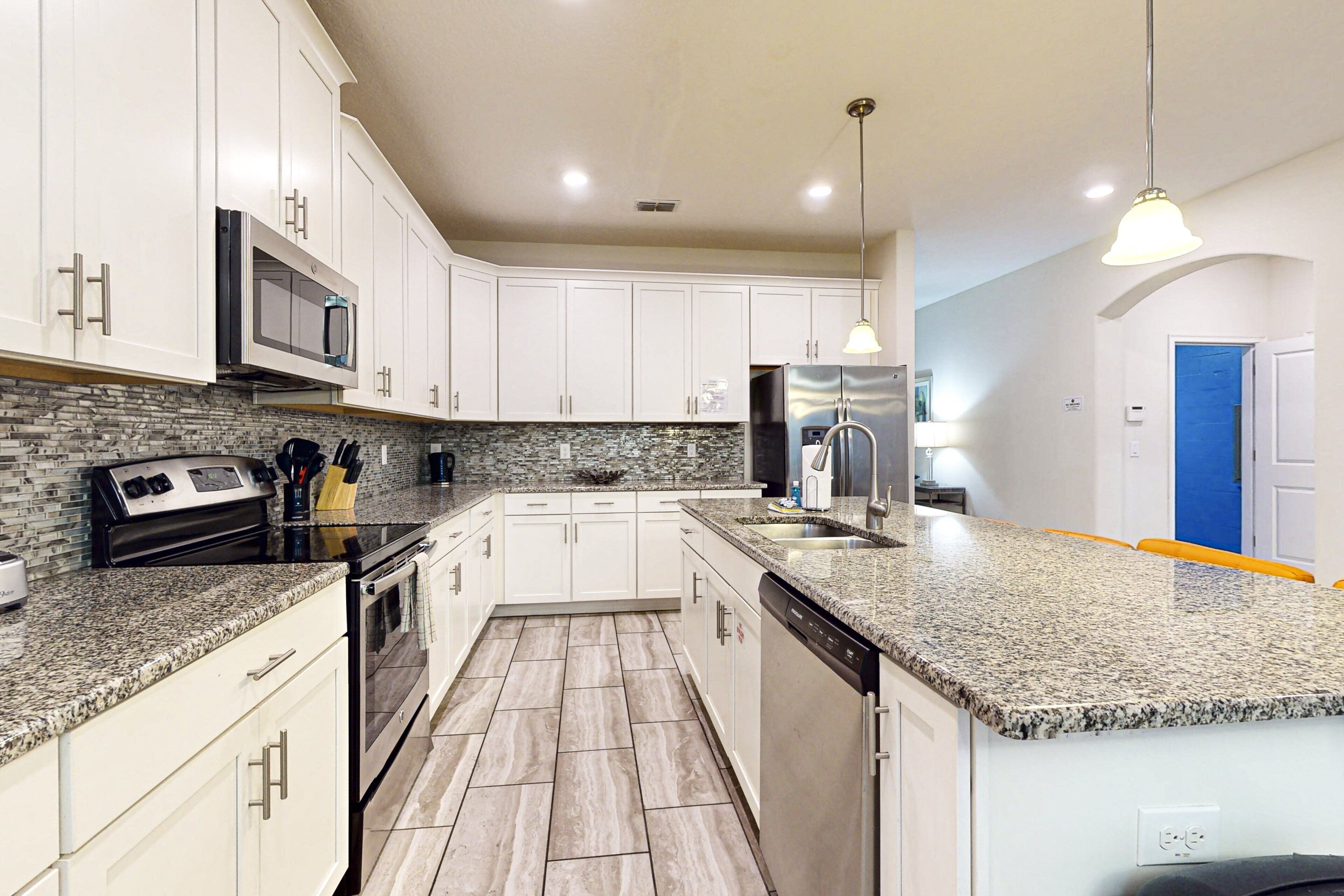 Una cocina moderna con armarios blancos, encimeras de granito, electrodomésticos de acero inoxidable y salpicadero de azulejos.