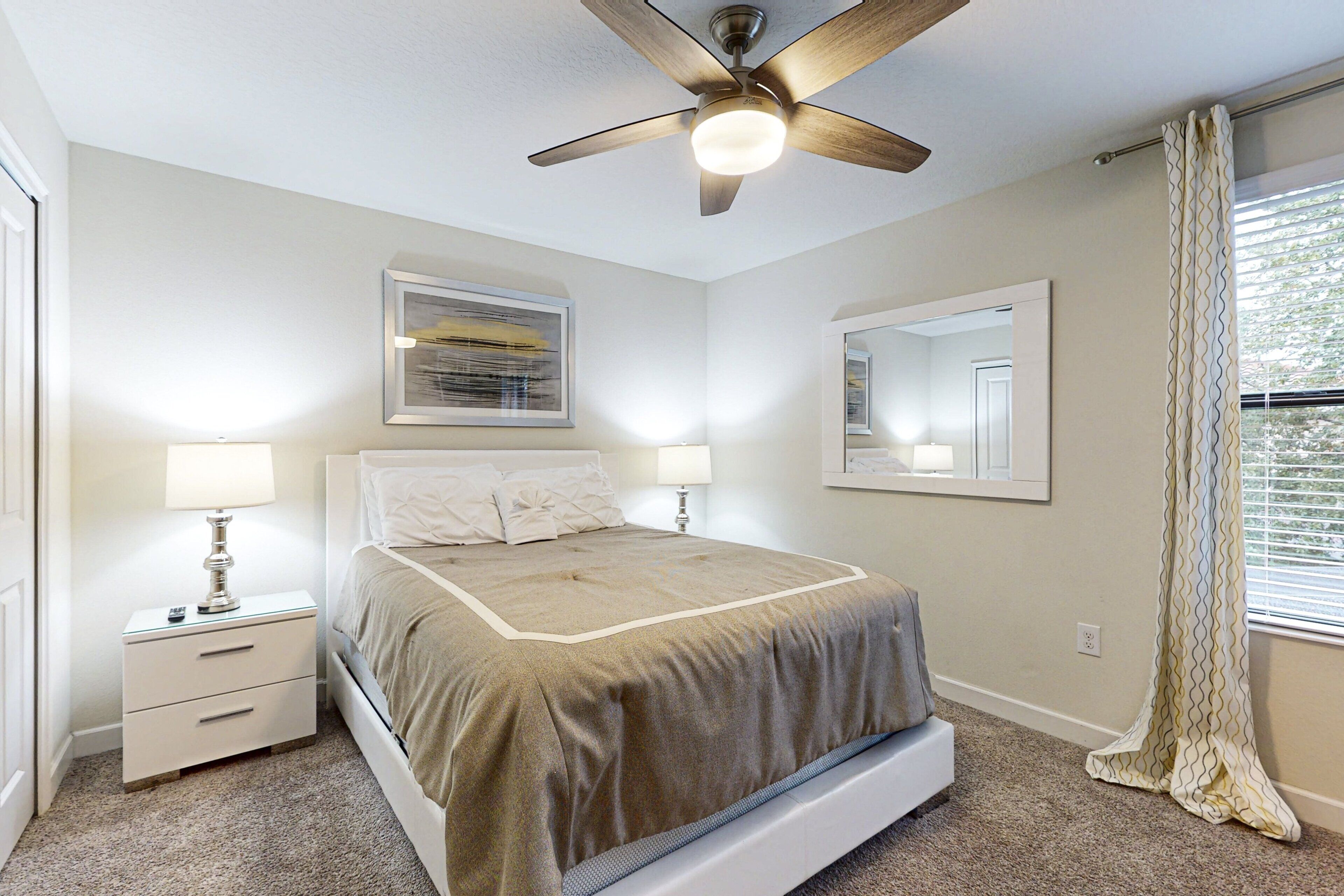 A bedroom with a bed, nightstands, a ceiling fan, and a window with curtains.