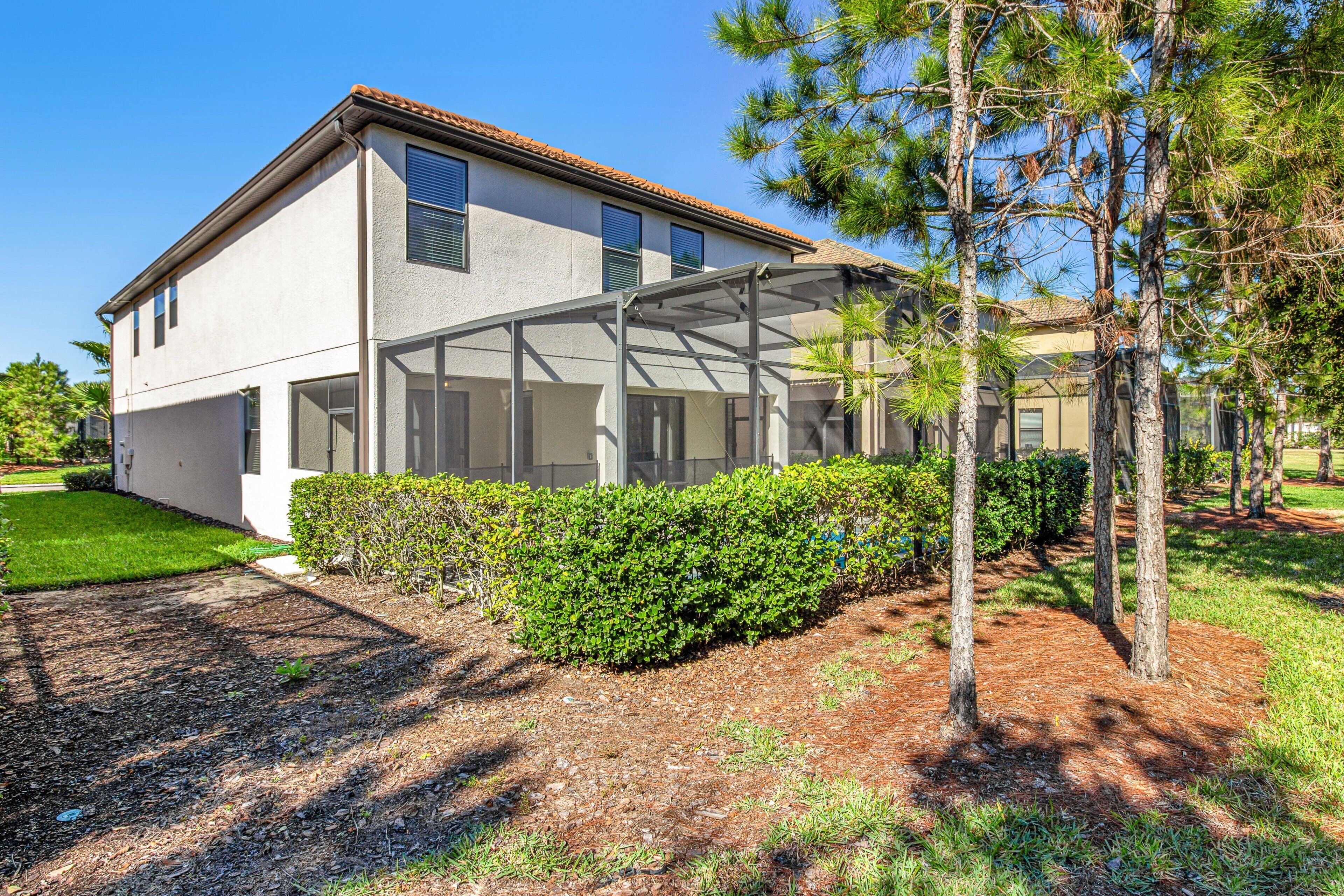 A two-story house with a covered patio area, a well-maintained lawn, and a pine tree.