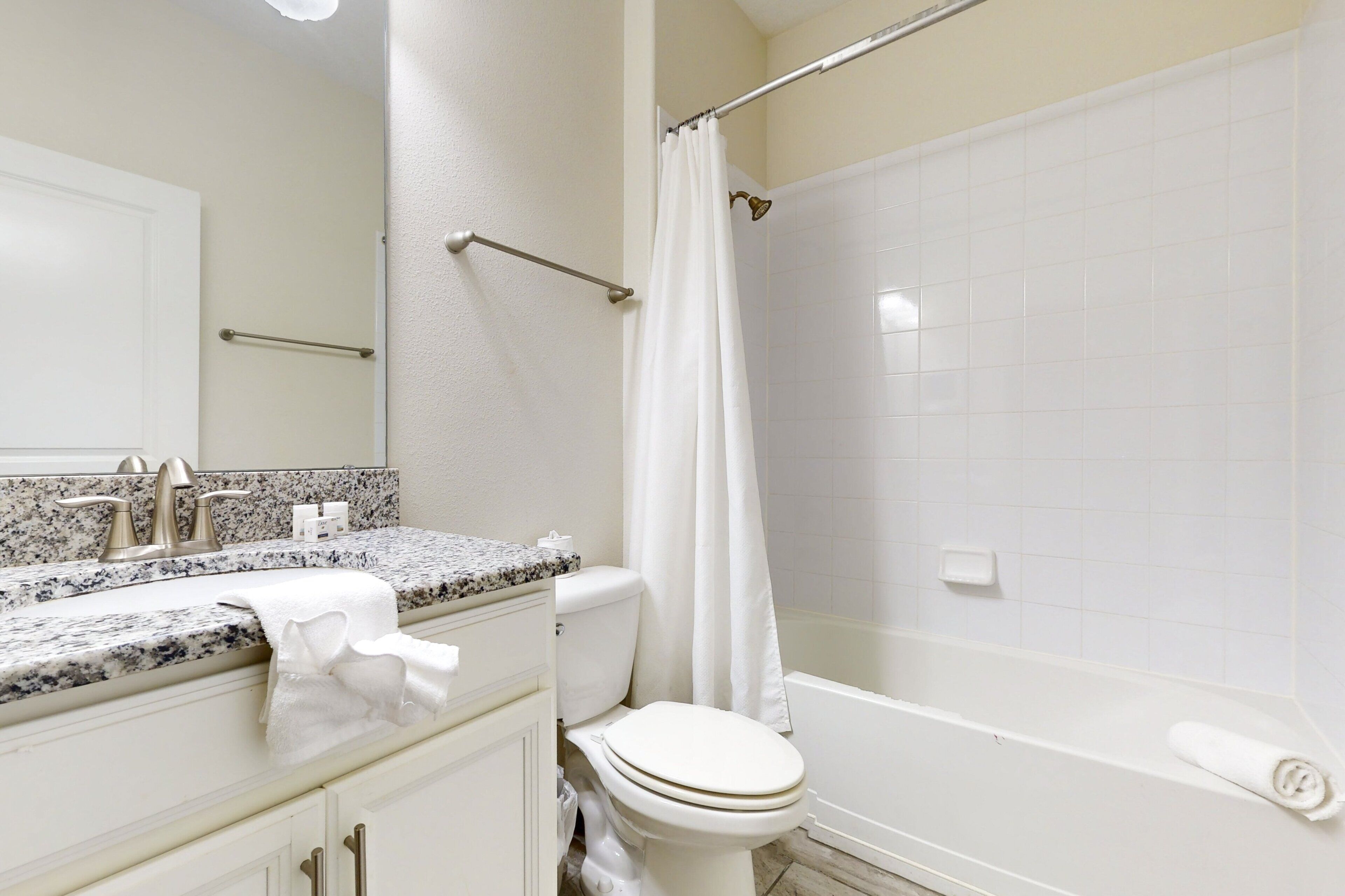 Un bagno con un WC bianco, una vasca, una tenda da doccia, un asciugamano sul pavimento e un lavabo con piano in marmo.