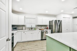 A modern kitchen with white cabinets, stainless steel appliances, and a green accent wall. - Dog-friendly Lakefront Home With Fast Wifi, Central AC, Patio, & Game Room (Sebring)
