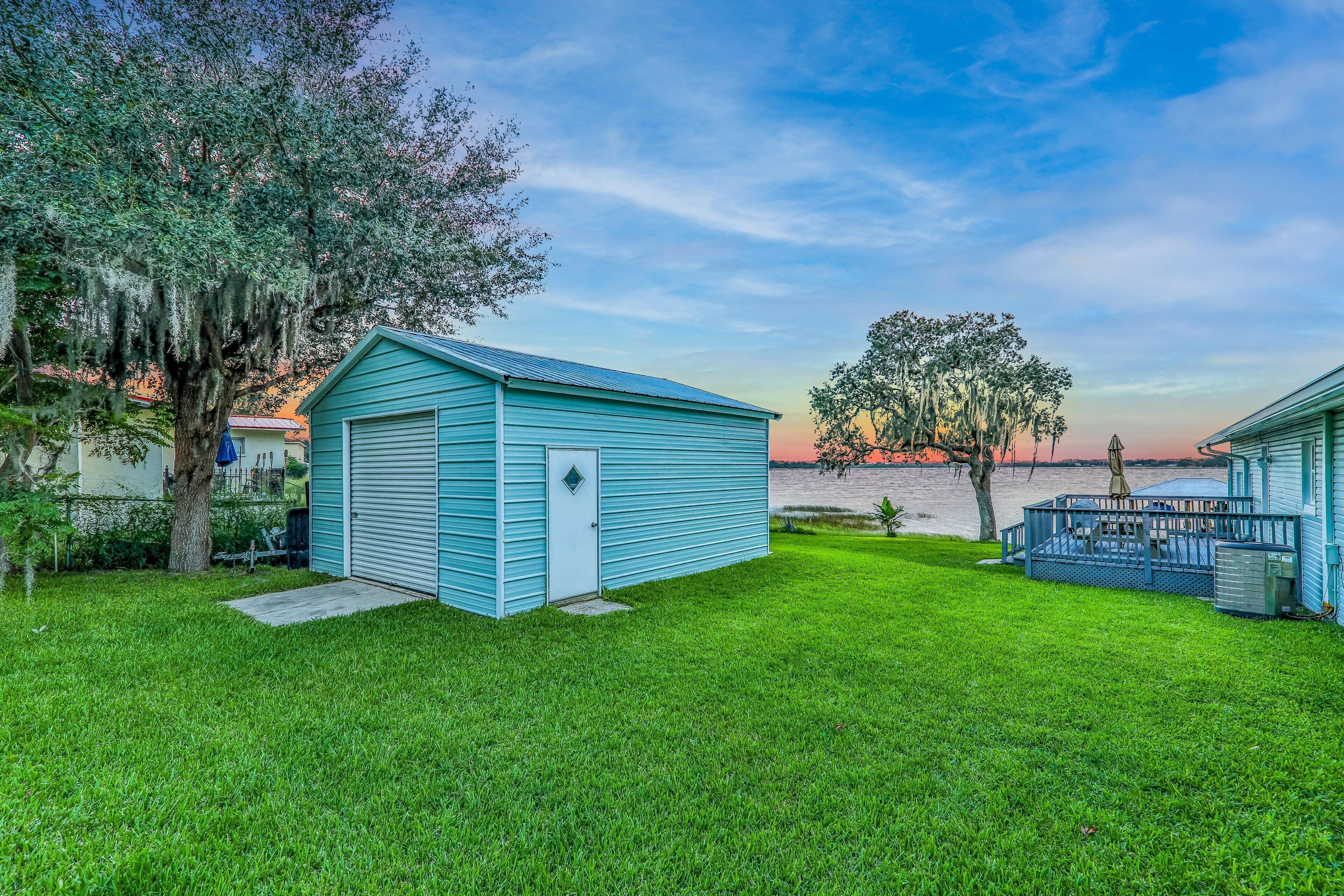 A house with a blue shed, a tree, and a view of the water.