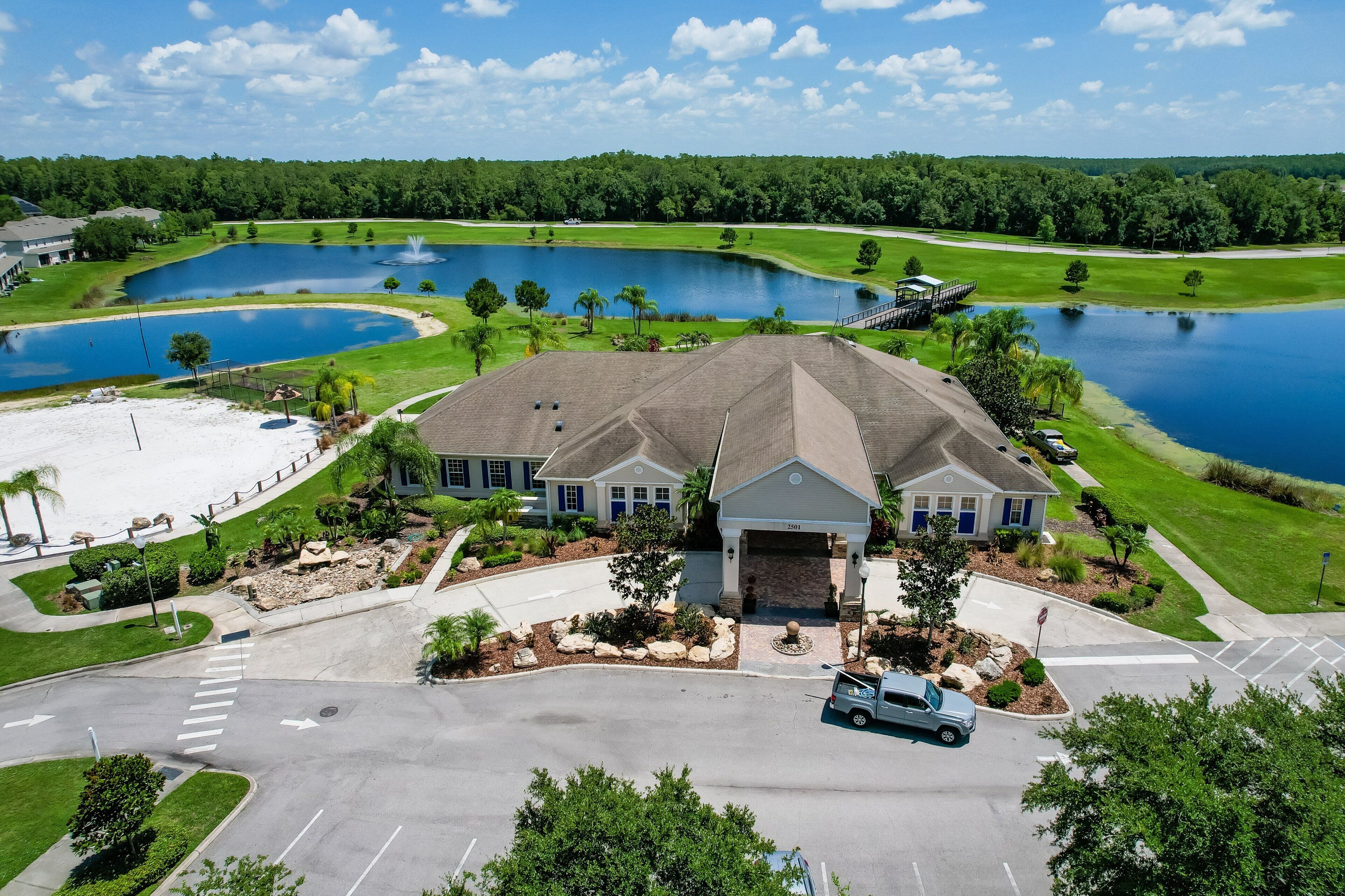 A large building with a driveway, a parking area, and a golf course with ponds in the background.