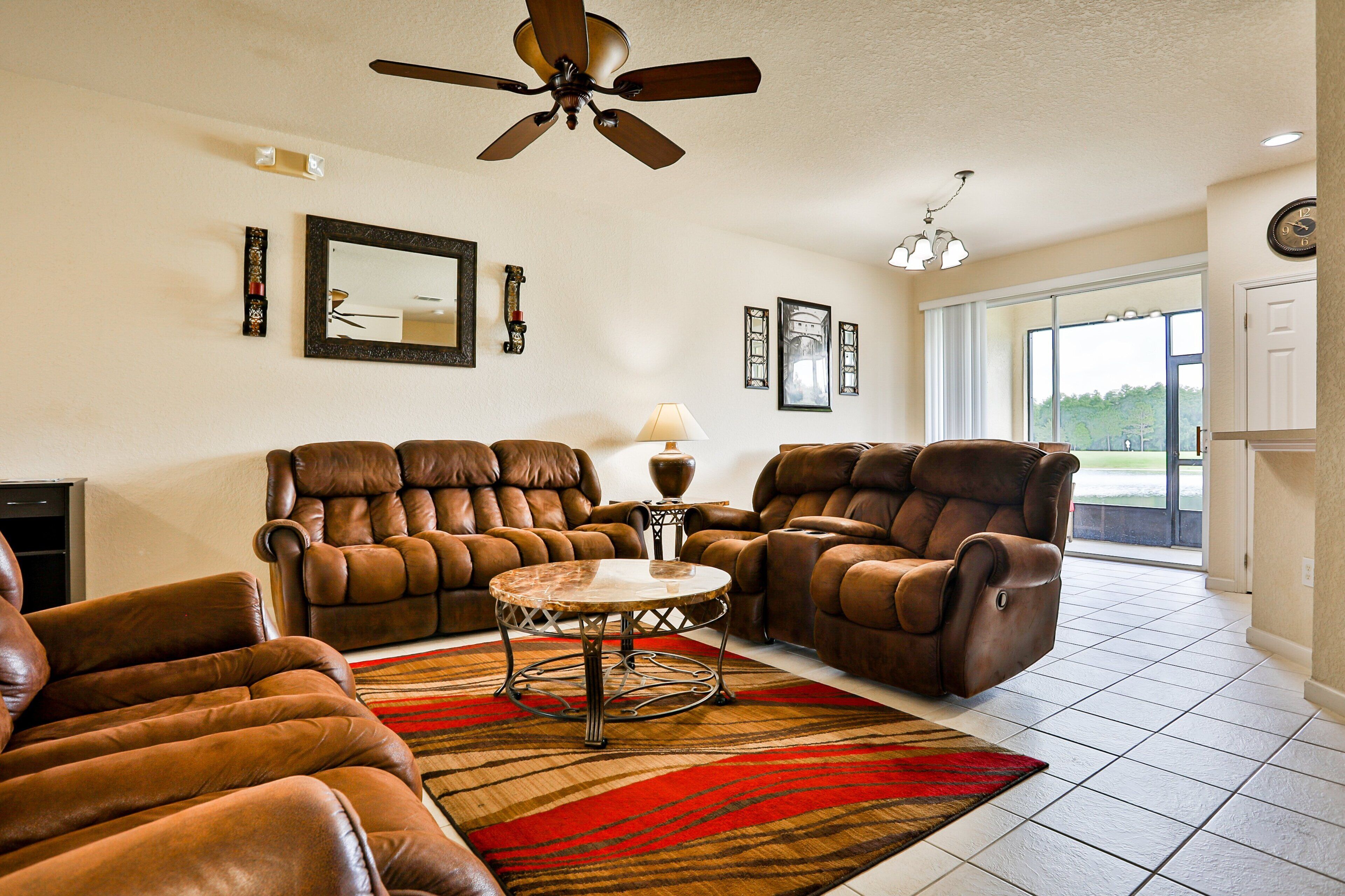 A living room with leather recliners, a round coffee table, and a ceiling fan.