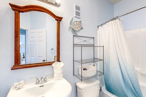 A bathroom with a white sink, a mirror with a wooden frame, a towel rack, a shower curtain, and a metal shelf unit. - Sunny Condo With Pool, hot Tub, Tennis Court, & gym - Balcony & Washer/dryer (Kissimmee)
