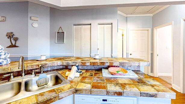 A kitchen with a stone countertop, stainless steel sink, and white cabinets. - Sunny Condo With Pool, hot Tub, Tennis Court, & gym - Balcony & Washer/dryer (Kissimmee)