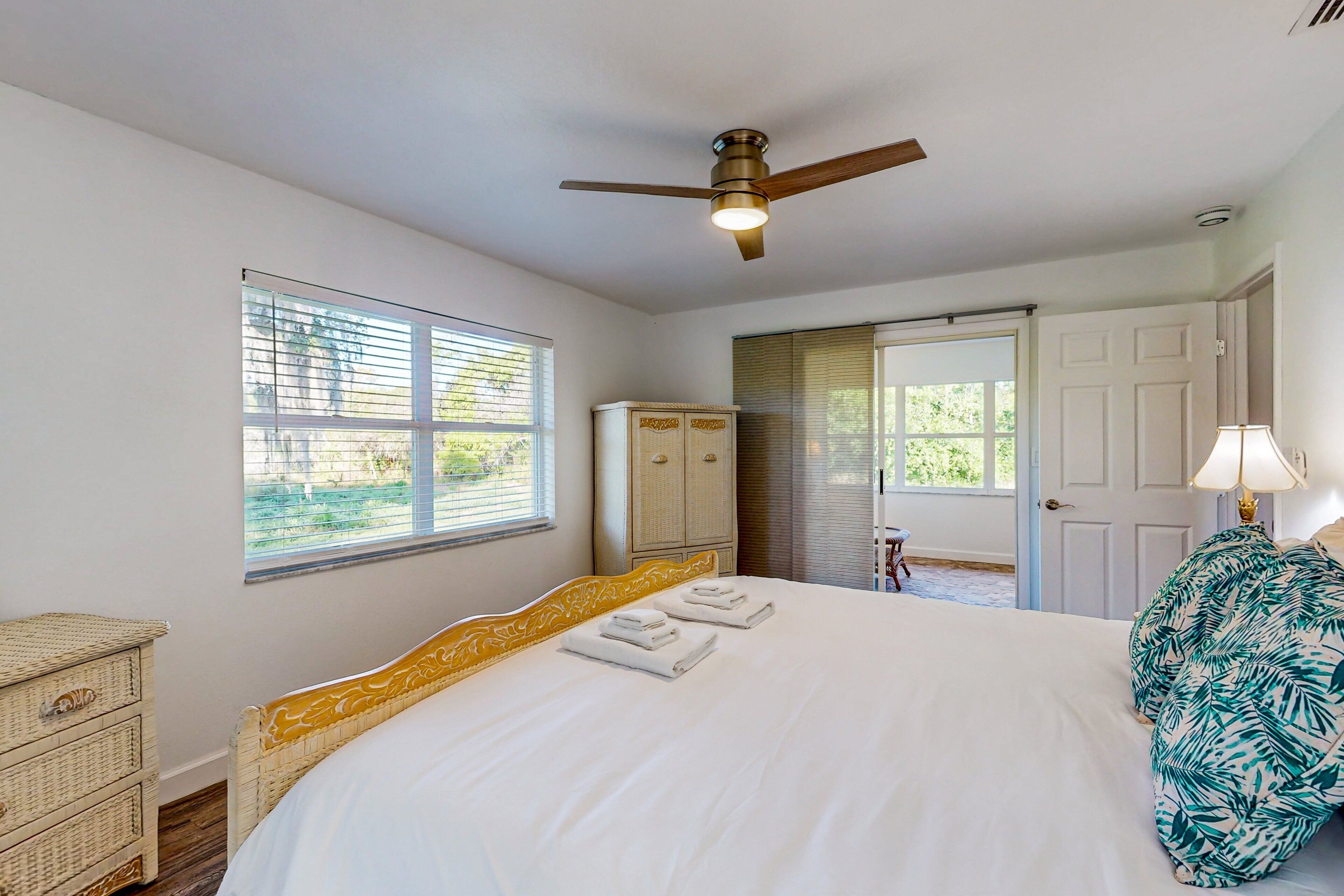 A bedroom with a bed, a ceiling fan, a wardrobe, and a door leading outside.