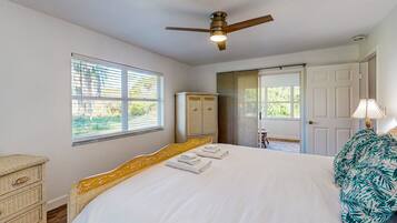 A bedroom with a bed, a ceiling fan, a wardrobe, and a door leading outside.