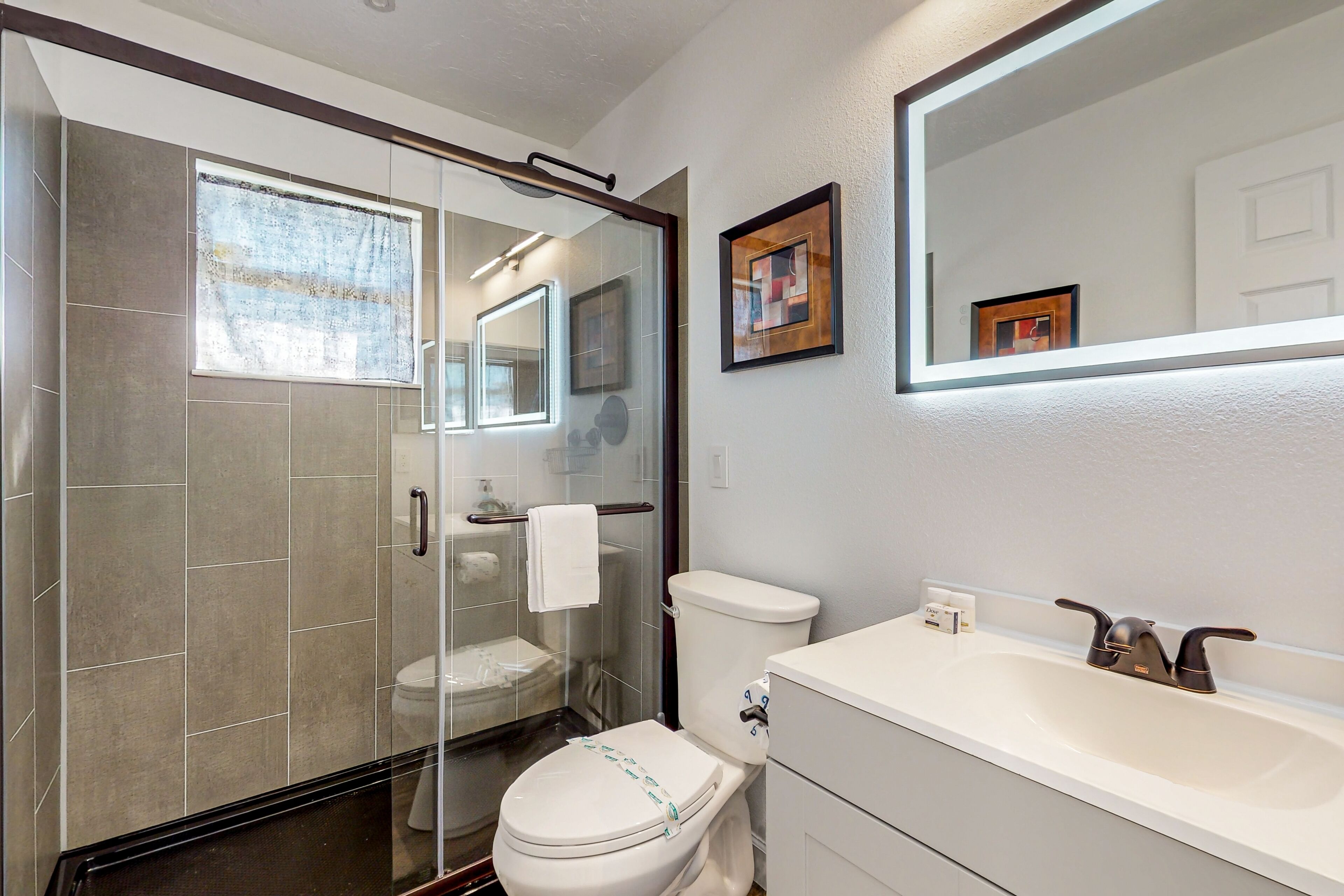 A modern bathroom with a glass shower enclosure, a white toilet, and a white sink with a mirror above.