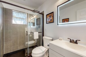 Ein modernes Badezimmer mit Duschkabine aus Glas, Toilette in Weiß und Waschbecken mit Spiegel darüber.