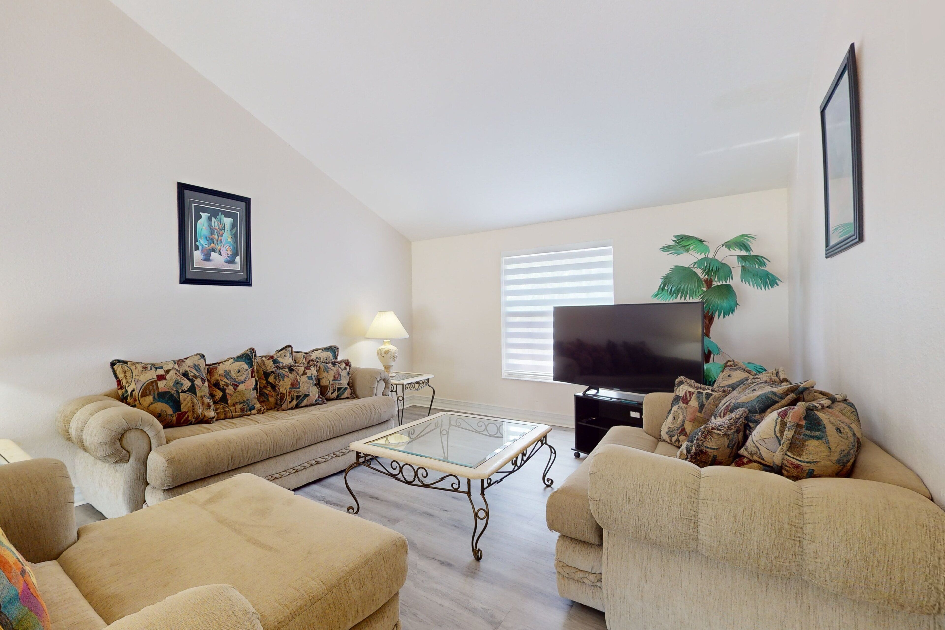 A living room with a sofa, armchair, coffee table, TV, lamp, and a plant.