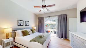 Une chambre à coucher comprenant un lit, des lampes de chevet, un ventilateur de plafond, une porte-fenêtre coulissante donnant sur un balcon et une commode.