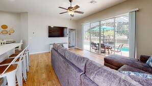 Un salon moderne comprenant un canapé, une table à manger, des chaises, un ventilateur de plafond et un téléviseur.