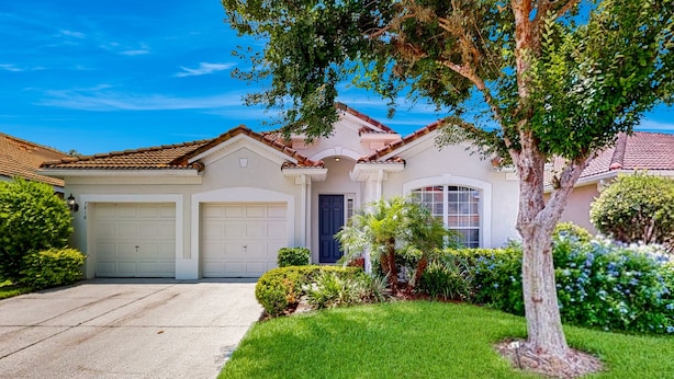 A residential house with a garage, a front lawn, and a tree. - All-suite Retreat With Pool, Spa, Waterslides, Tennis - Near Dining & Disney (Kissimmee)