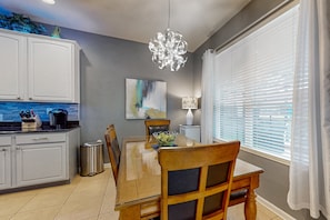 A dining area with a wooden table, chairs, a chandelier, a painting, and a window with blinds. - All-suite Retreat With Pool, Spa, Waterslides, Tennis - Near Dining & Disney (Kissimmee)
