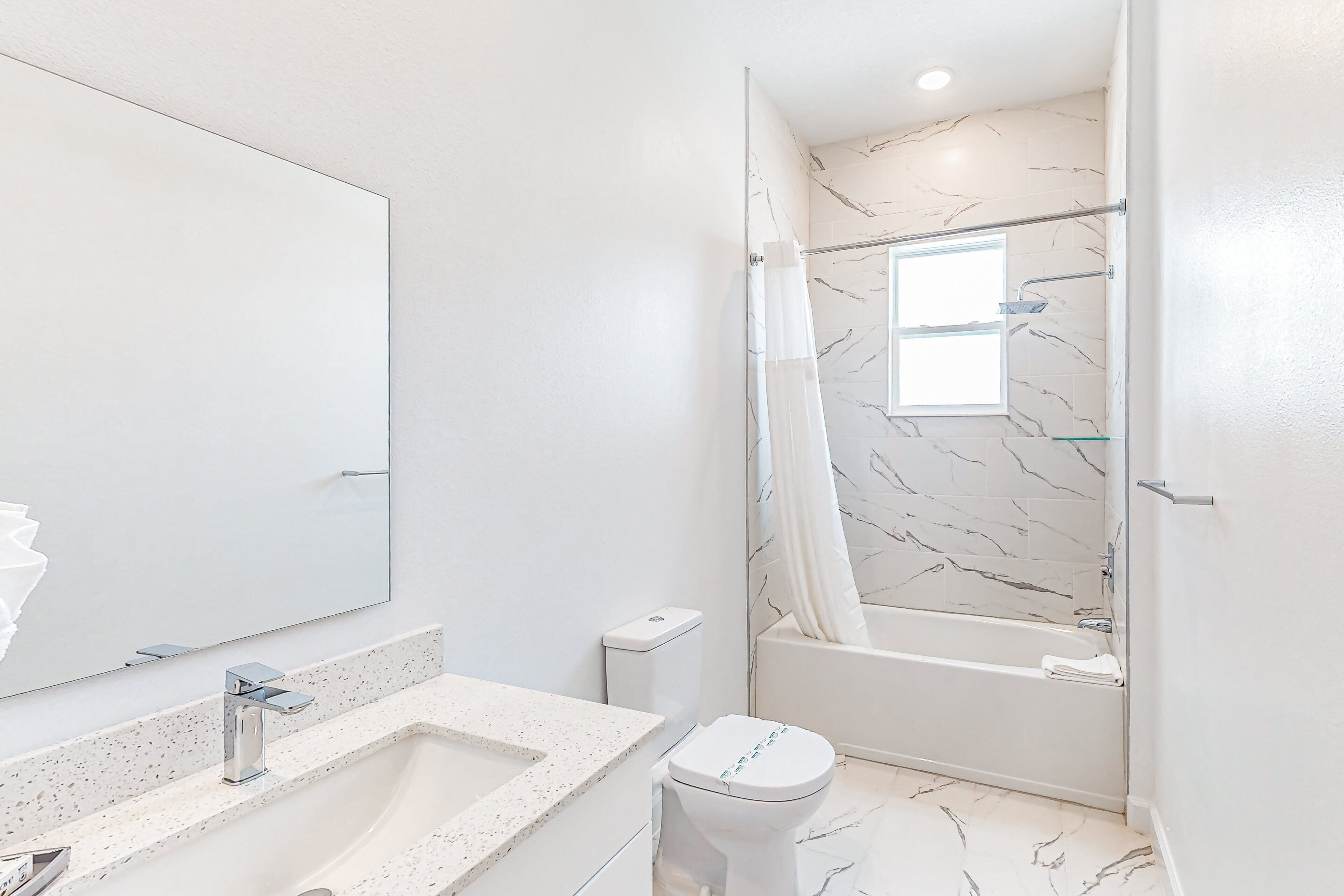 A bathroom with a large mirror, a sink, a toilet, and a shower area.