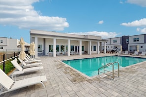 A swimming pool with lounge chairs and umbrellas, a covered seating area, and a modern building in the background. - Elegant Townhouse With a Private Pool, Lanai, & Washer/dryer - Dog-friendly (Davenport)
