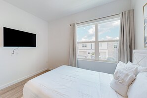 A hotel room with a bed, a TV mounted on the wall, a window with curtains, and a view of buildings outside. - Elegant Townhouse With a Private Pool, Lanai, & Washer/dryer - Dog-friendly (Davenport)