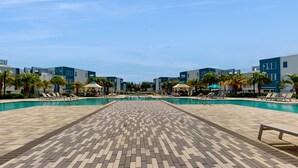 A pool area with tiled flooring, lounge chairs, and modern buildings in the background. - Golf Course-front Condo With Golf Views, Balcony, Pool, Fast Wifi, Washer/dryer (Kissimmee)
