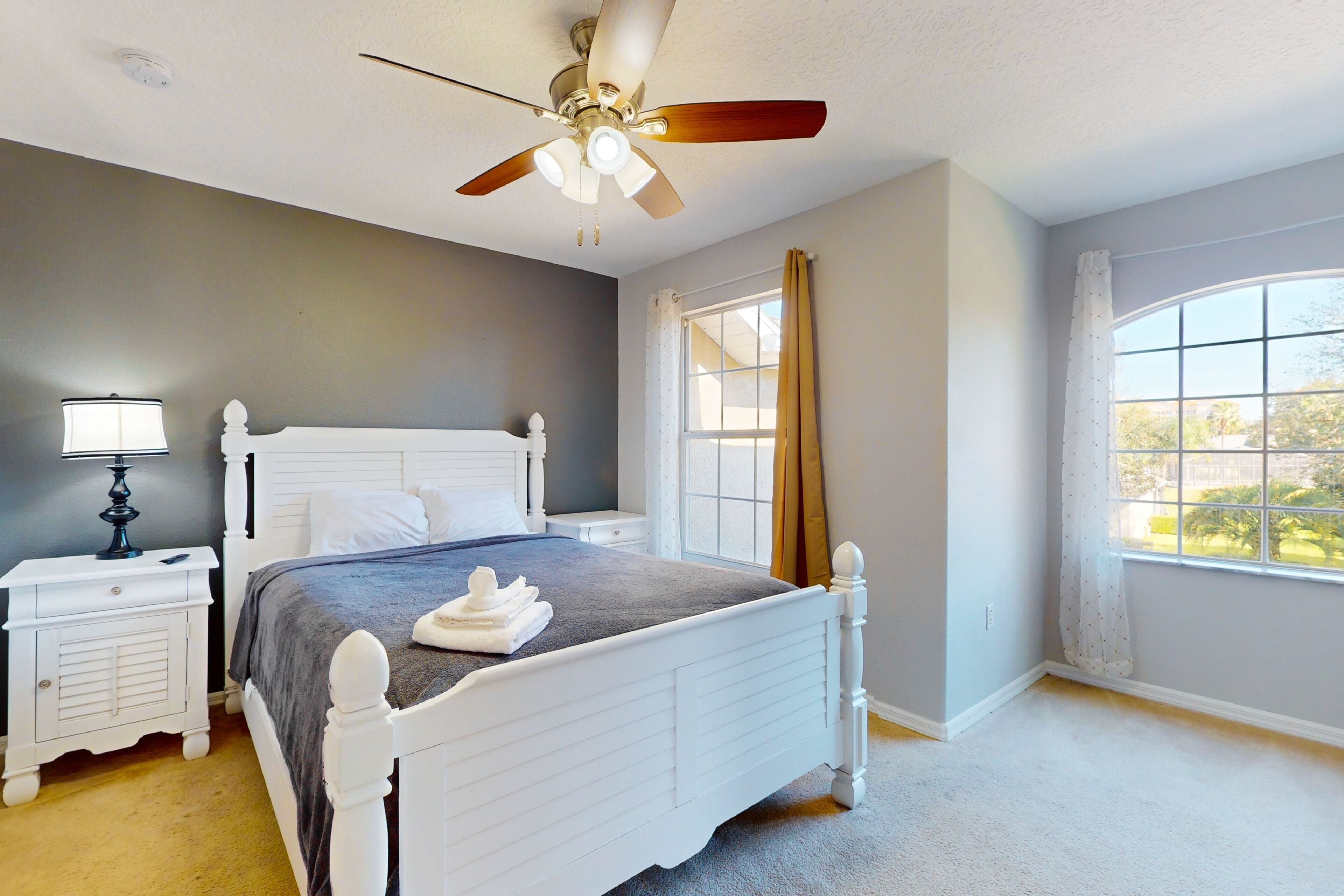 A bedroom with a bed, nightstands, a ceiling fan, and a large window with curtains.