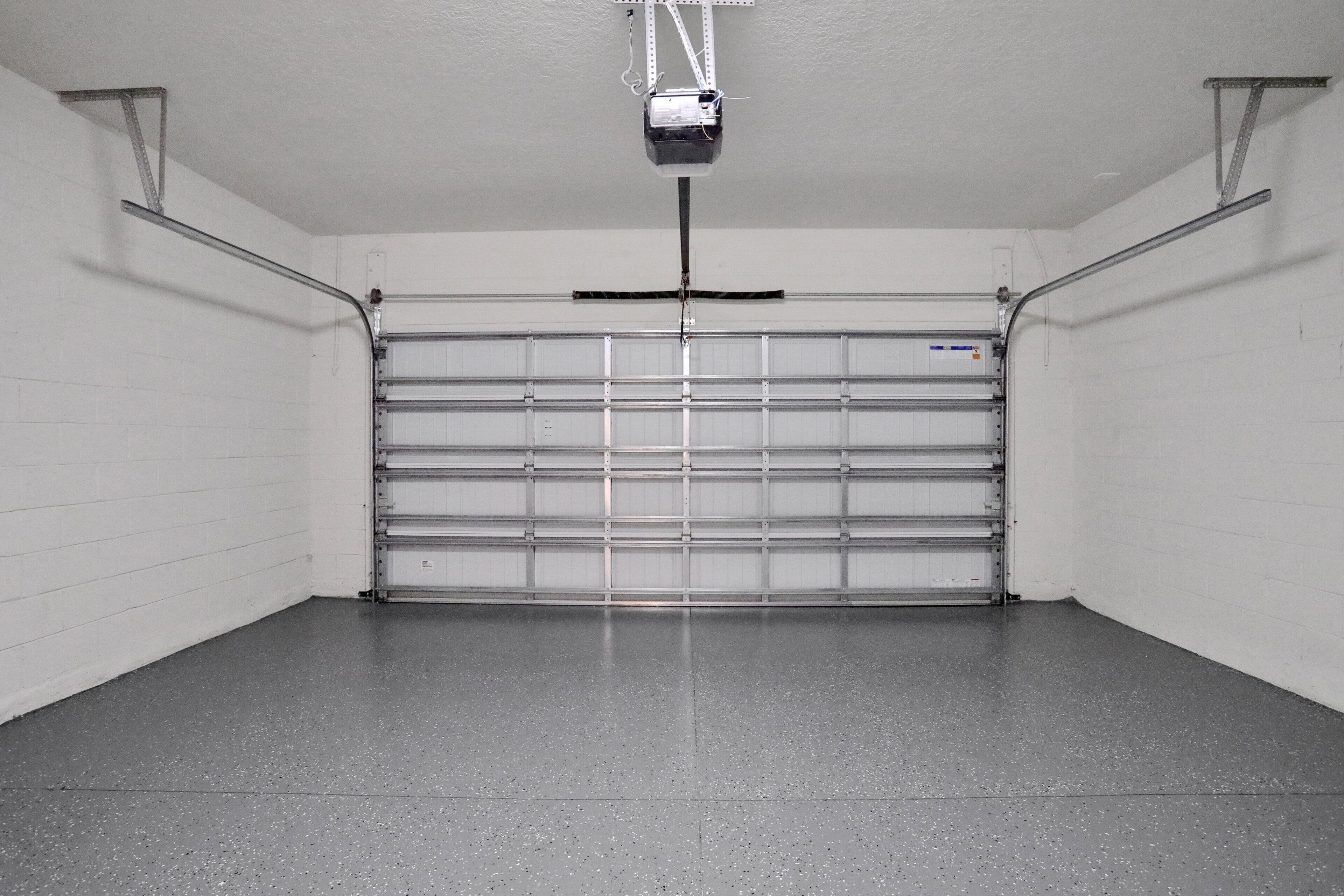 Un garage con una porta metallica chiusa, un pavimento in cemento e un proiettore montato a soffitto.