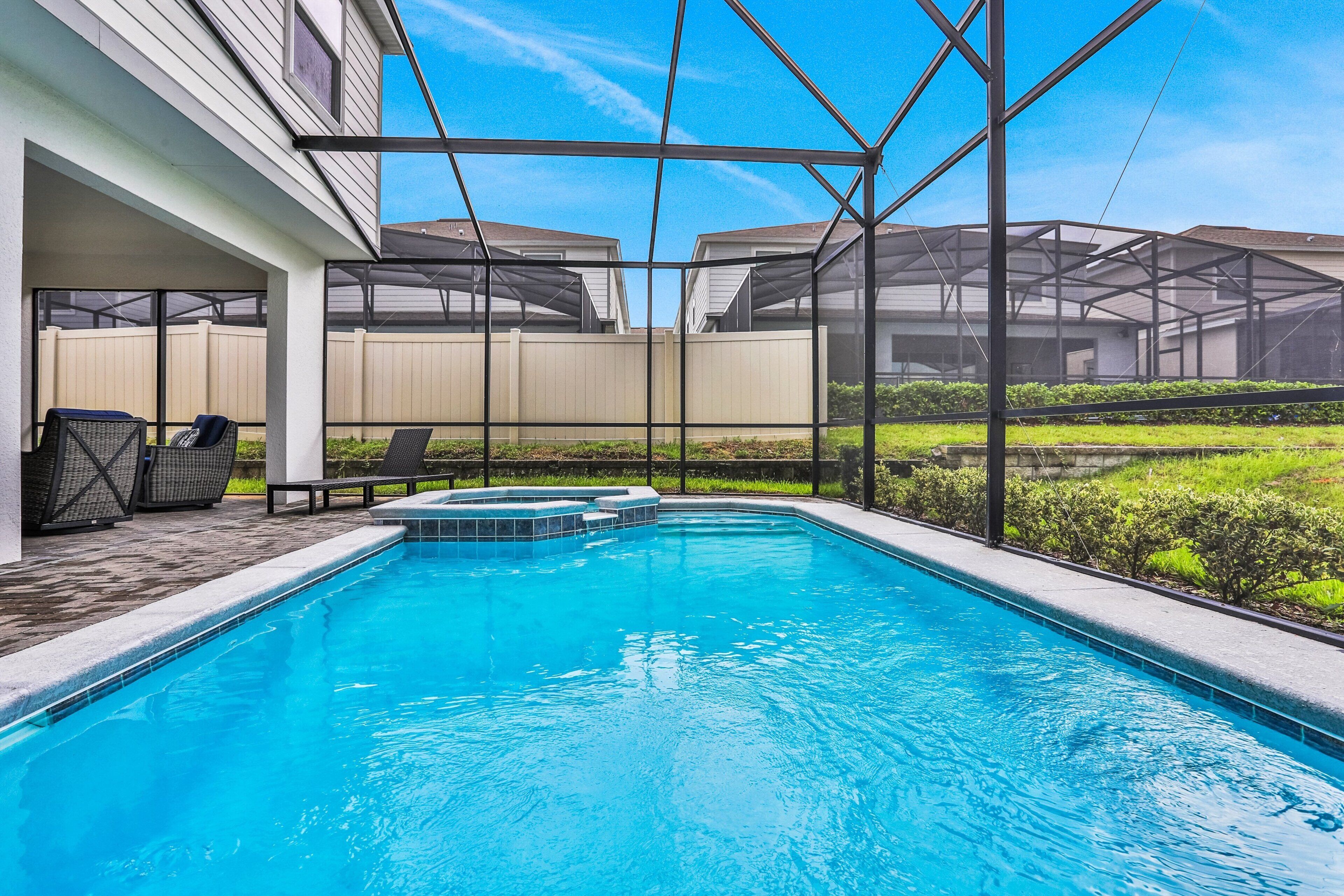 A swimming pool with a hot tub, covered seating area, and a view of a residential neighborhood.