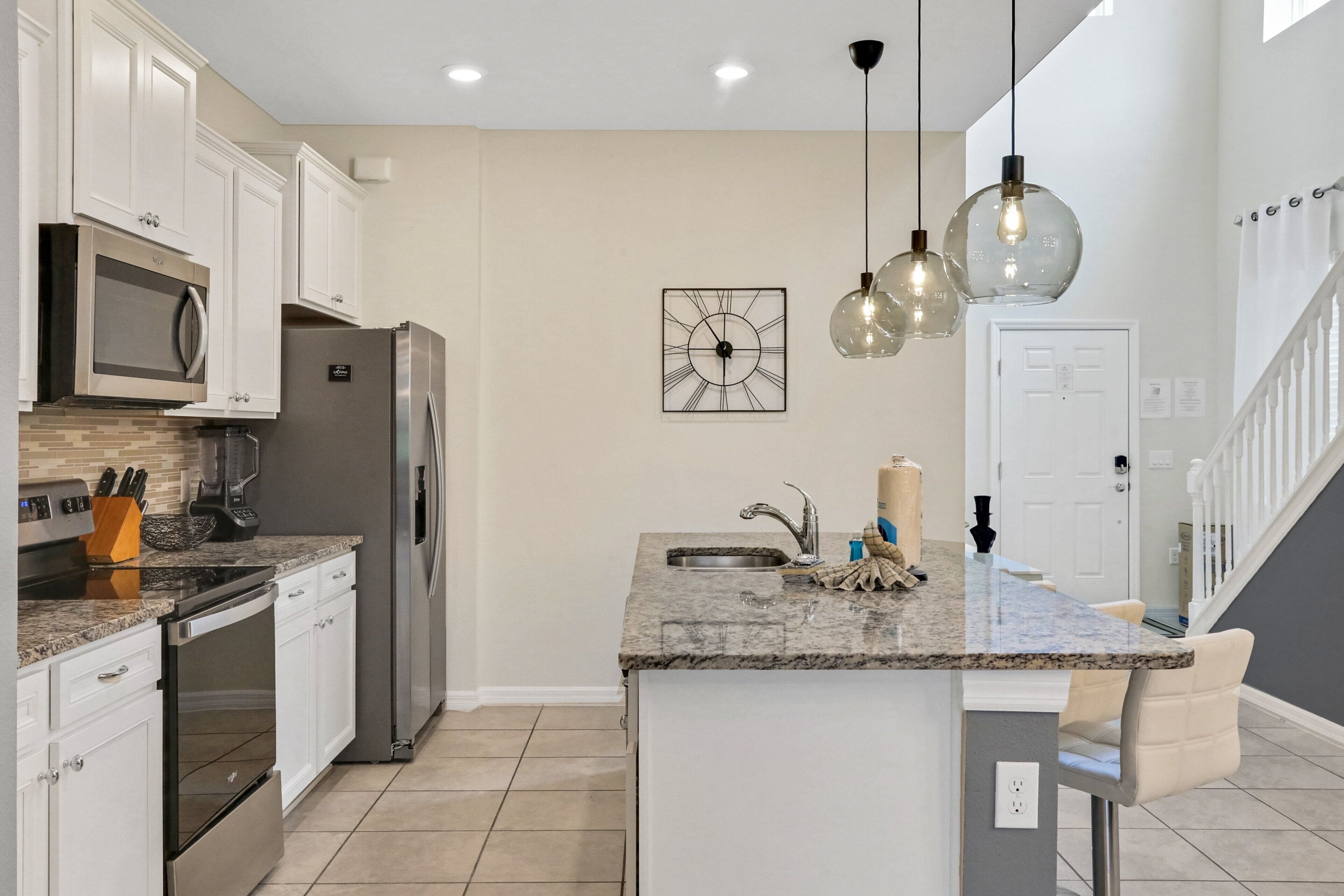 A modern kitchen with white cabinets, stainless steel appliances, a granite countertop, and pendant lighting.