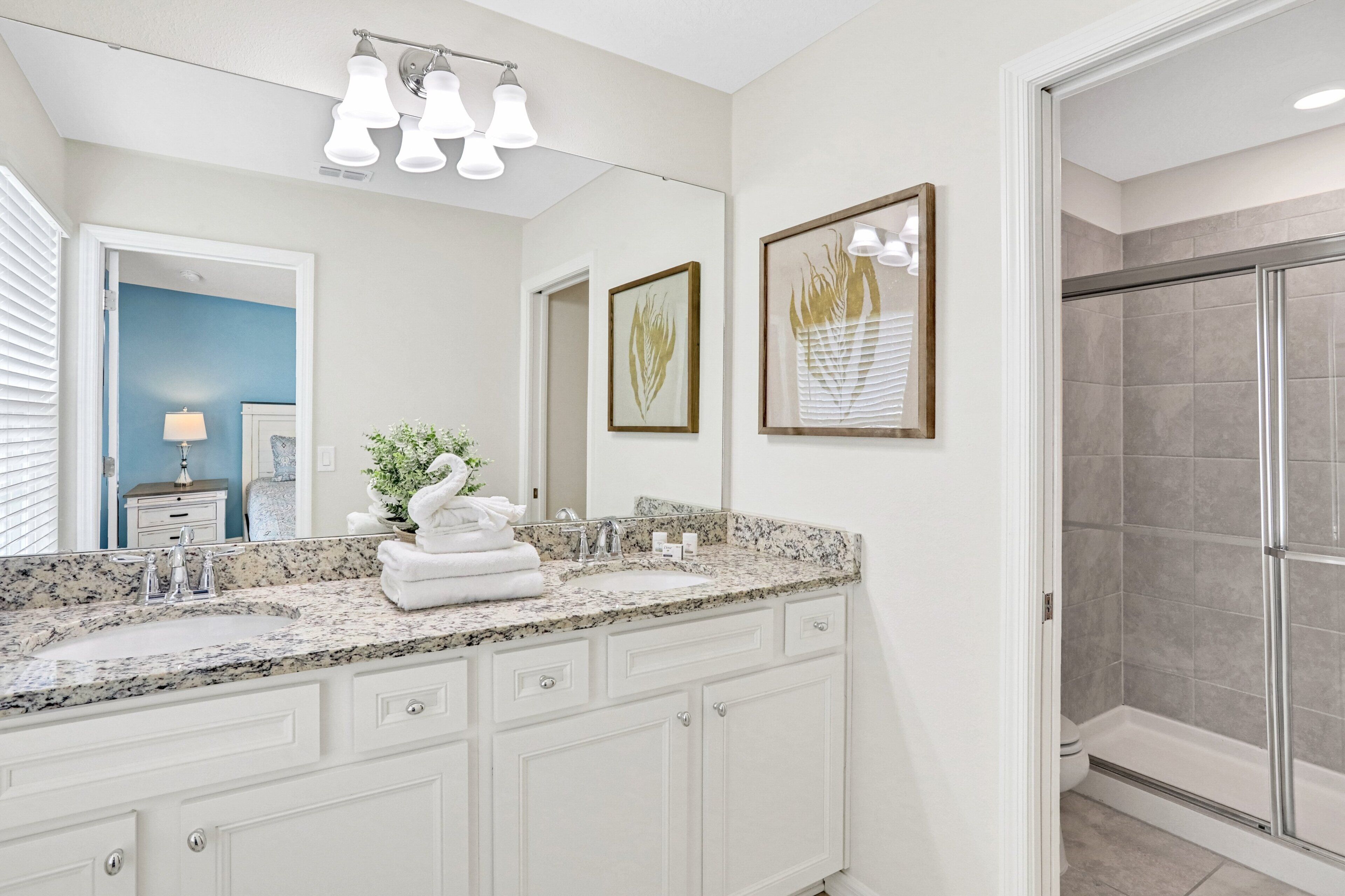 A bathroom with a granite countertop, white cabinets, a large mirror, and a shower area.