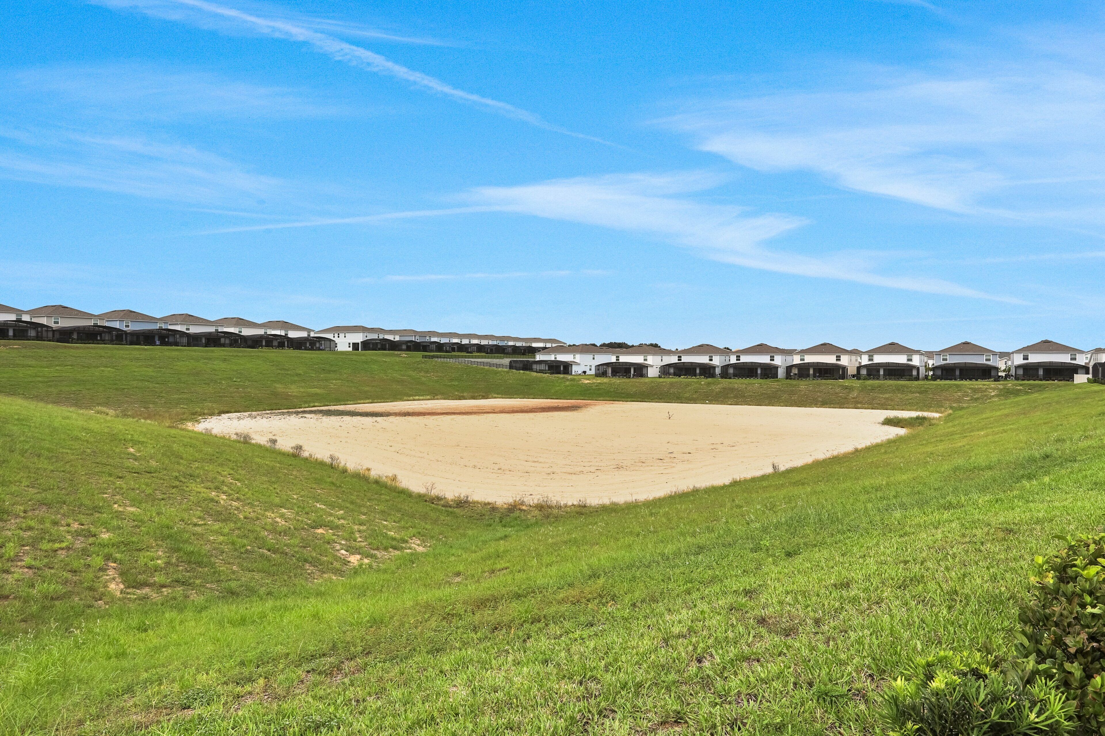 A golf course with bunkers and a sand trap, surrounded by a row of white buildings with brown roofs.