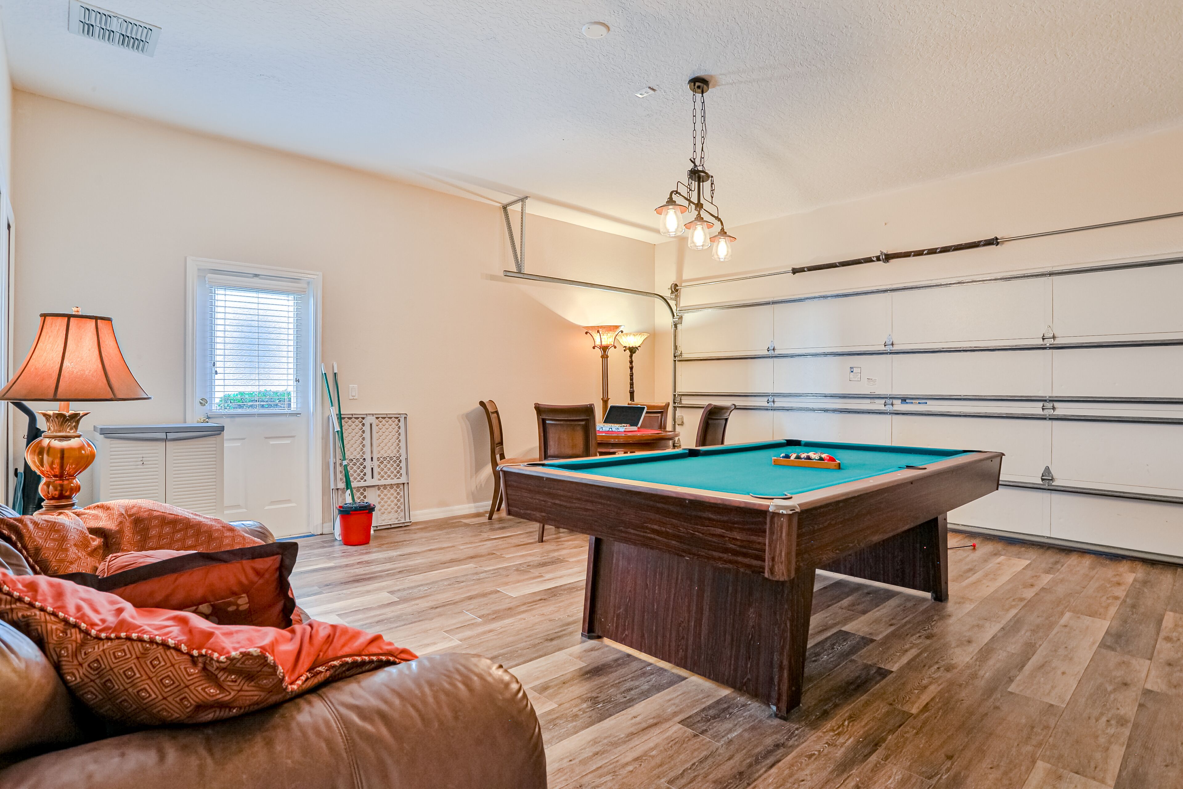 A pool table in a room with a wooden floor, a lamp, and a chair.