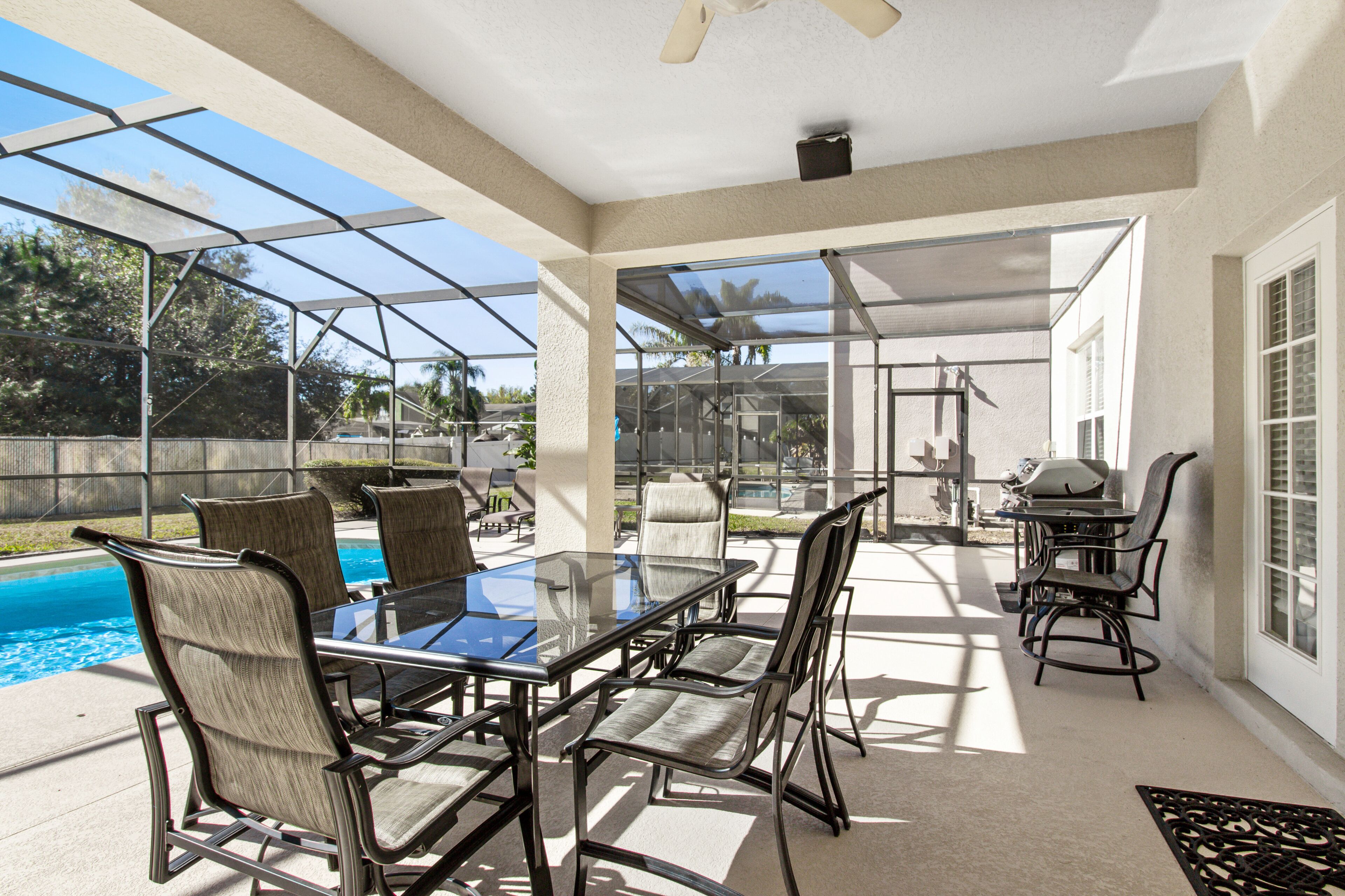 Un patio couvert avec une table et des chaises en verre, une piscine et un espace barbecue.