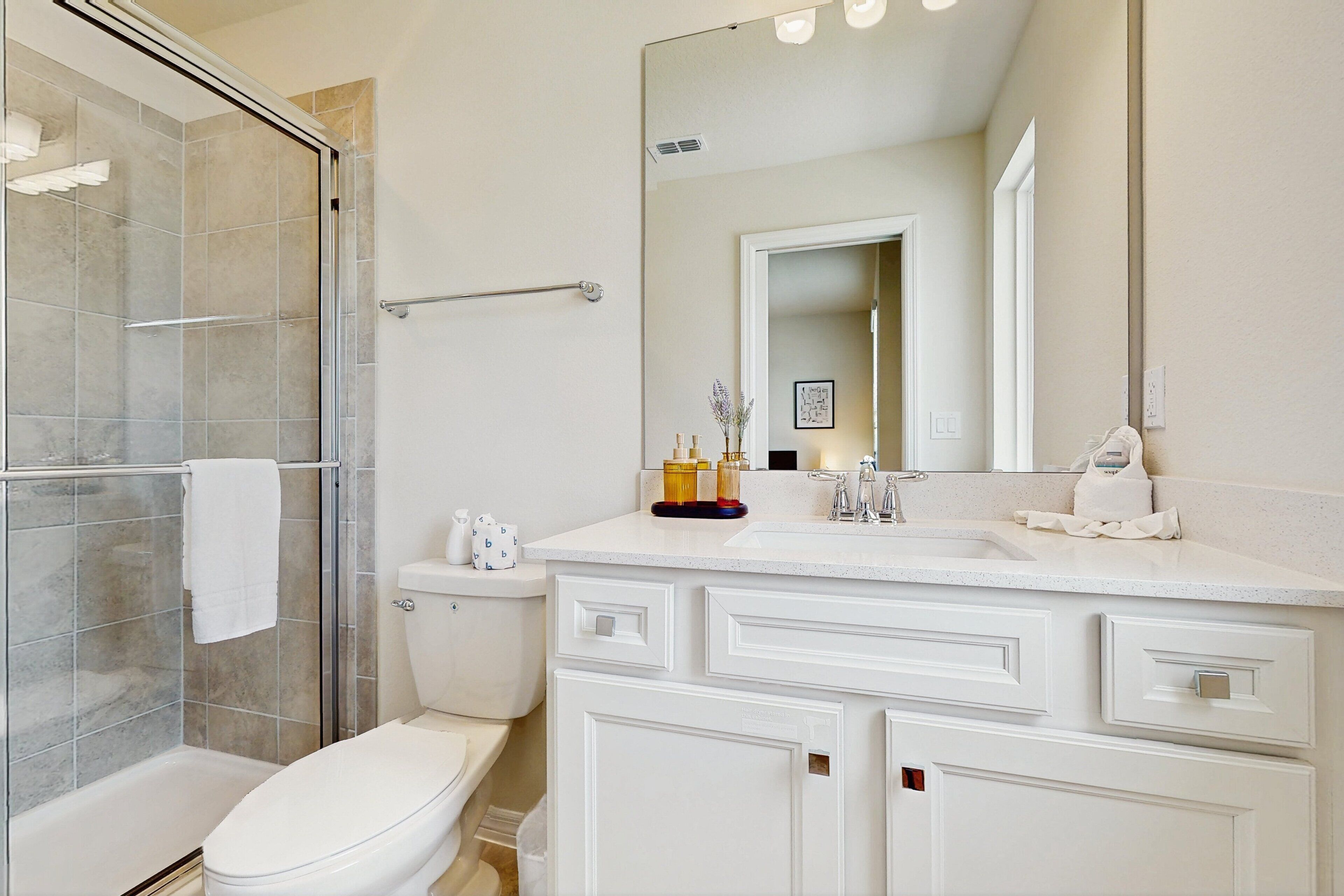 A bathroom with a glass shower enclosure, a toilet, a sink with a mirror, and a vanity with drawers.