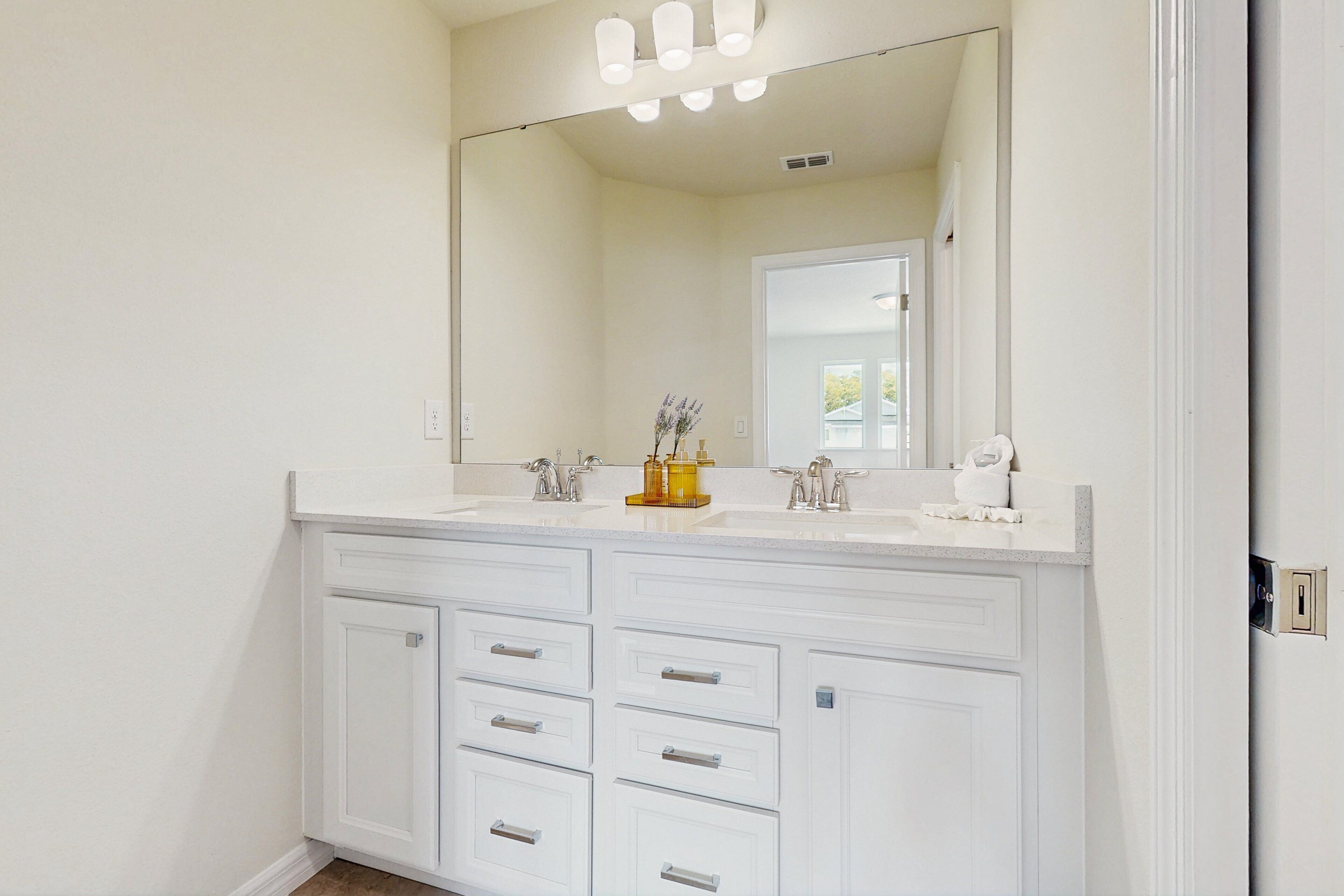 A white bathroom vanity with a large mirror, two sinks, and multiple drawers.