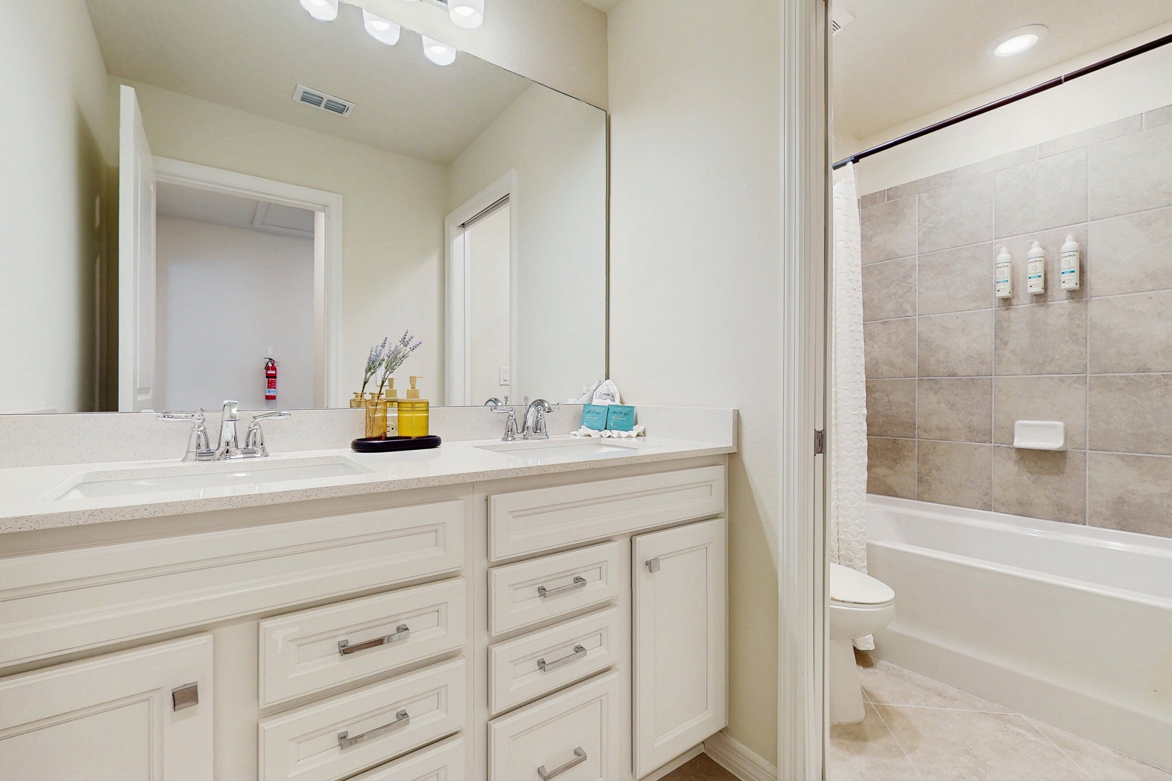 A bathroom with a double sink vanity, a mirror, a bathtub, and a toilet.