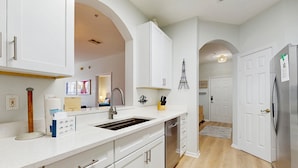 Una cocina moderna con muebles blancos, un lavamanos de acero inoxidable y un lavavajillas empotrado.