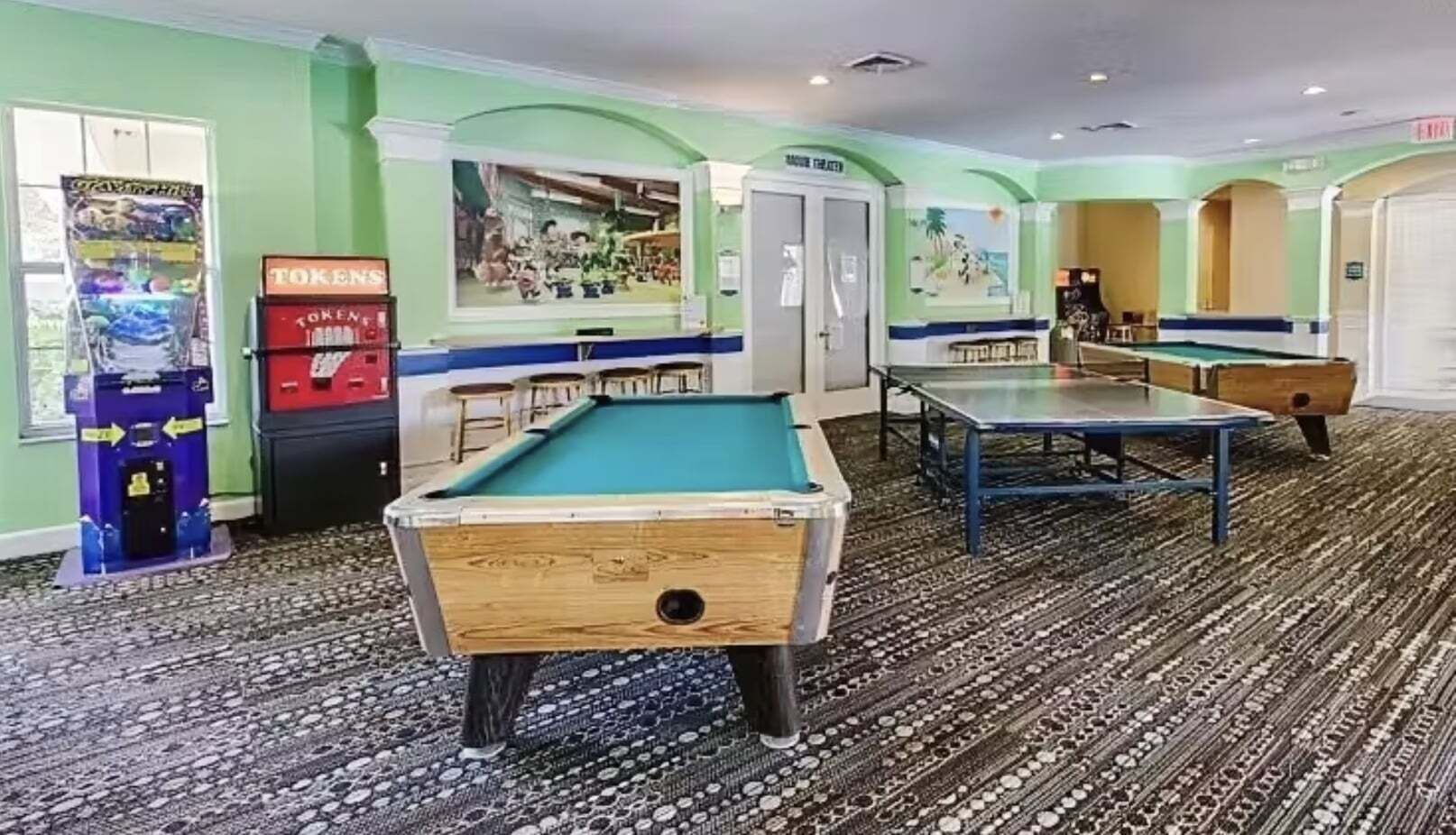 A pool table, a ping pong table, and a pool table in a room with patterned carpet.