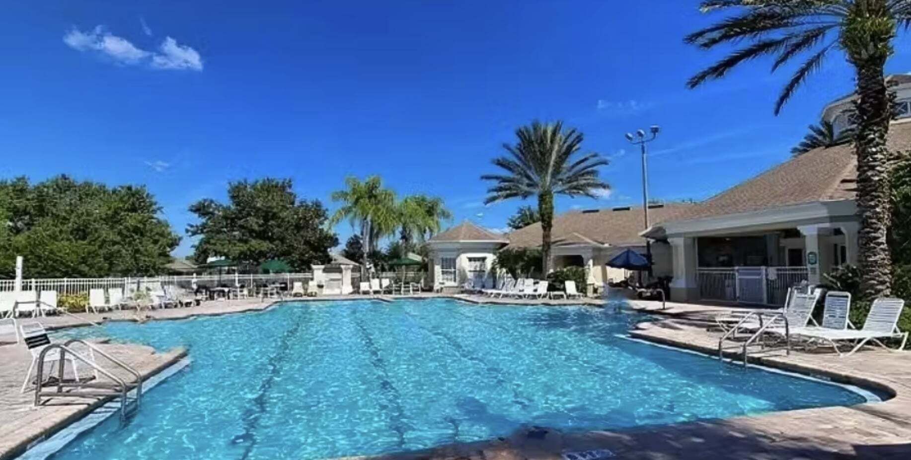 Piscina com espreguiçadeiras, palmeiras e céu azul límpido.