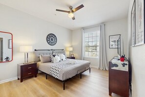 A bedroom with a bed, bedside lamps, a ceiling fan, a bedside table, a dresser, a window with blinds, and a wall decoration. - Beautiful Home With Resort Pool and Space for the Whole Family (Kissimmee)