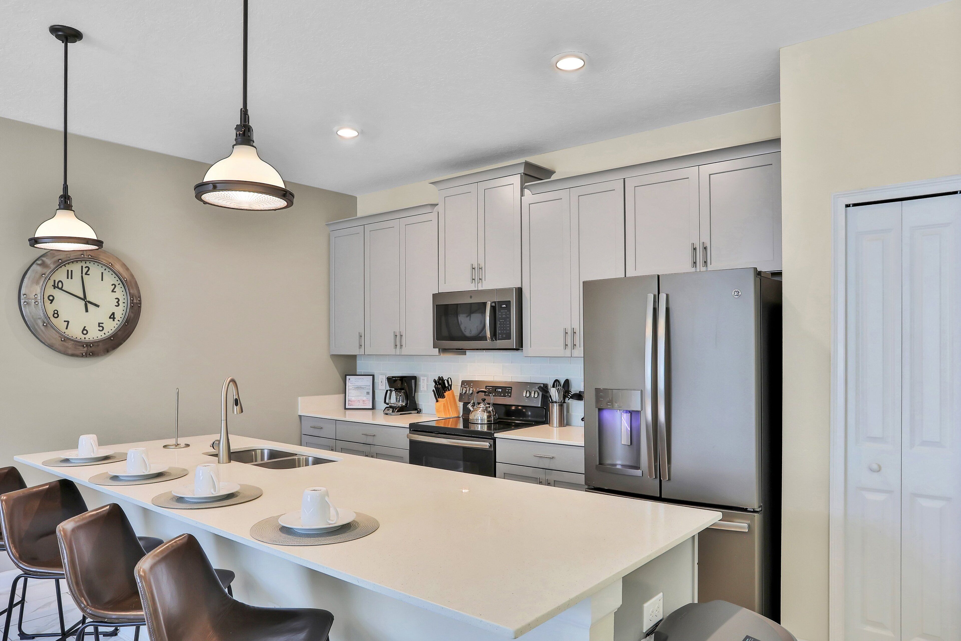 Une cuisine moderne dotée d’un îlot central, d’appareils électroménagers en acier inoxydable et de luminaires suspendus.