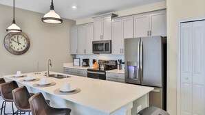 A modern kitchen with a central island, stainless steel appliances, and pendant lighting. - Modern Luxury Townhome With hot tub & Private Pool - Near Theme Parks (Davenport)