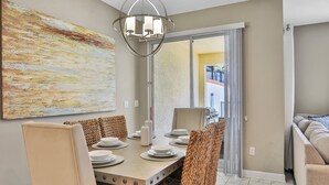 A dining area with a table set for four, chairs, a chandelier, and a large abstract painting on the wall. - Modern Luxury Townhome With hot tub & Private Pool - Near Theme Parks (Davenport)