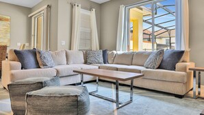 A living room with a sectional sofa, a coffee table, and a view through a large window. - Modern Luxury Townhome With hot tub & Private Pool - Near Theme Parks (Davenport)