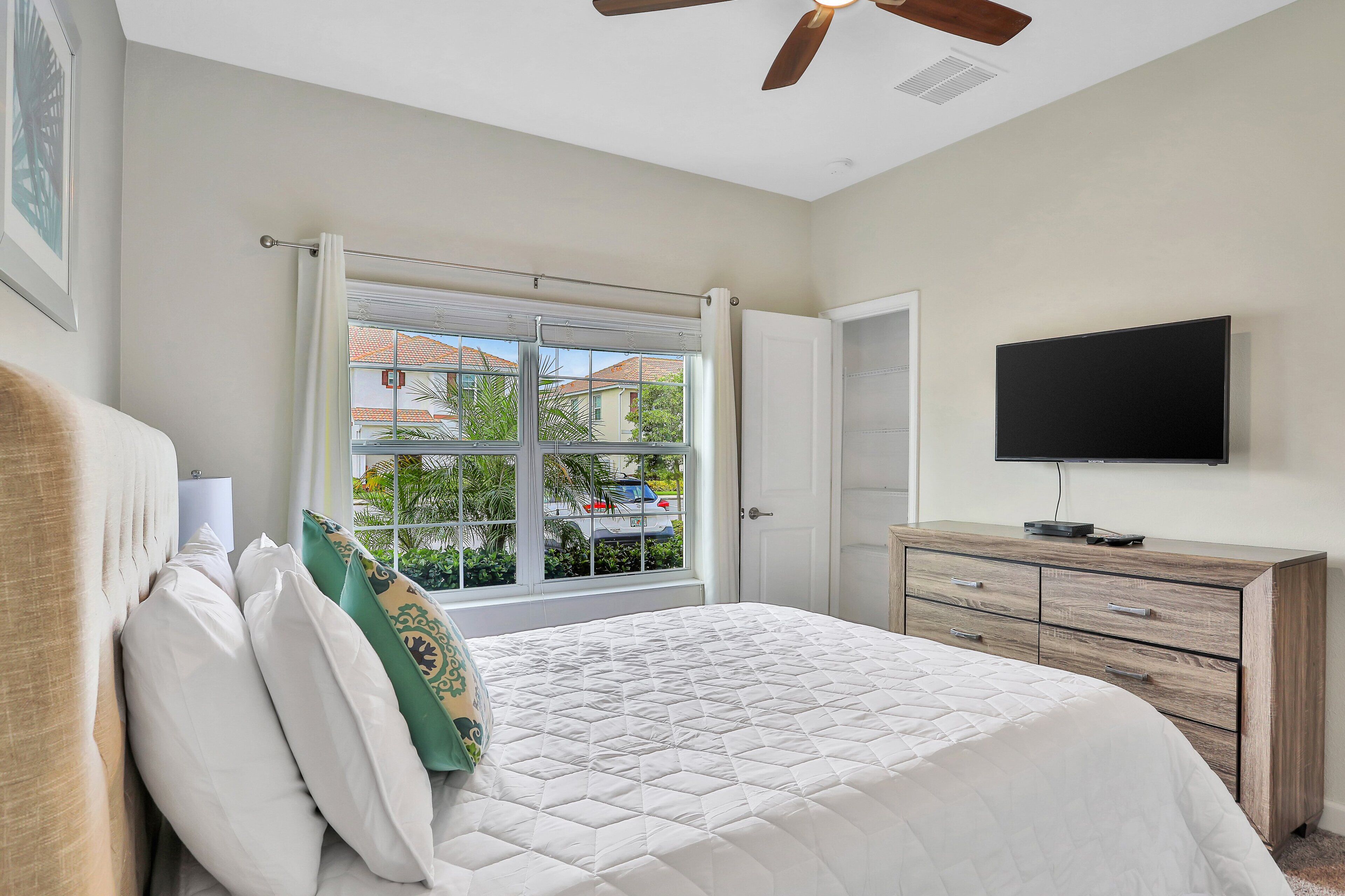 A bedroom with a bed, a television, a window with curtains, and a ceiling fan.