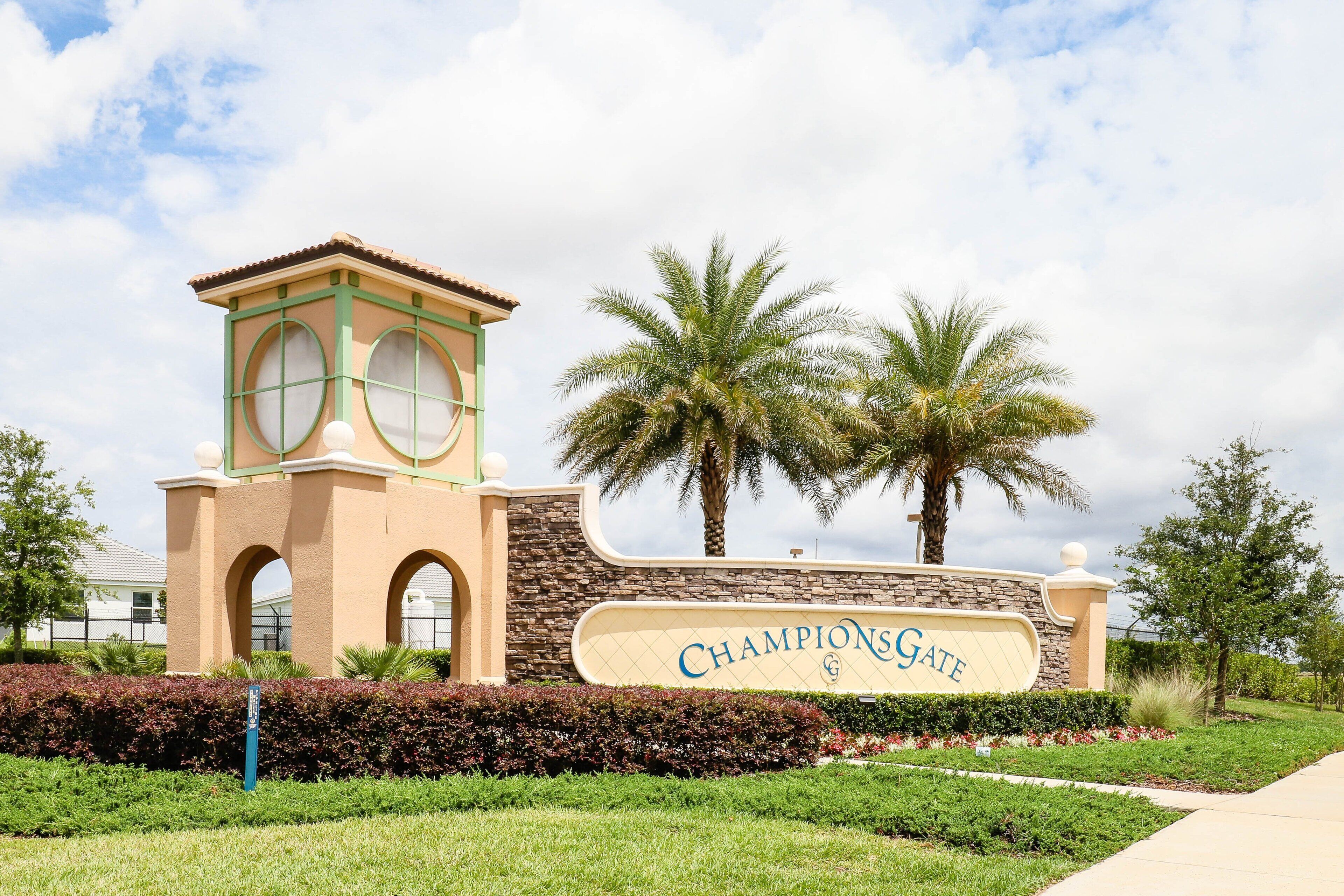 A building with a sign reading 'Champions Gate,' featuring a tower with arched windows and a stone facade.